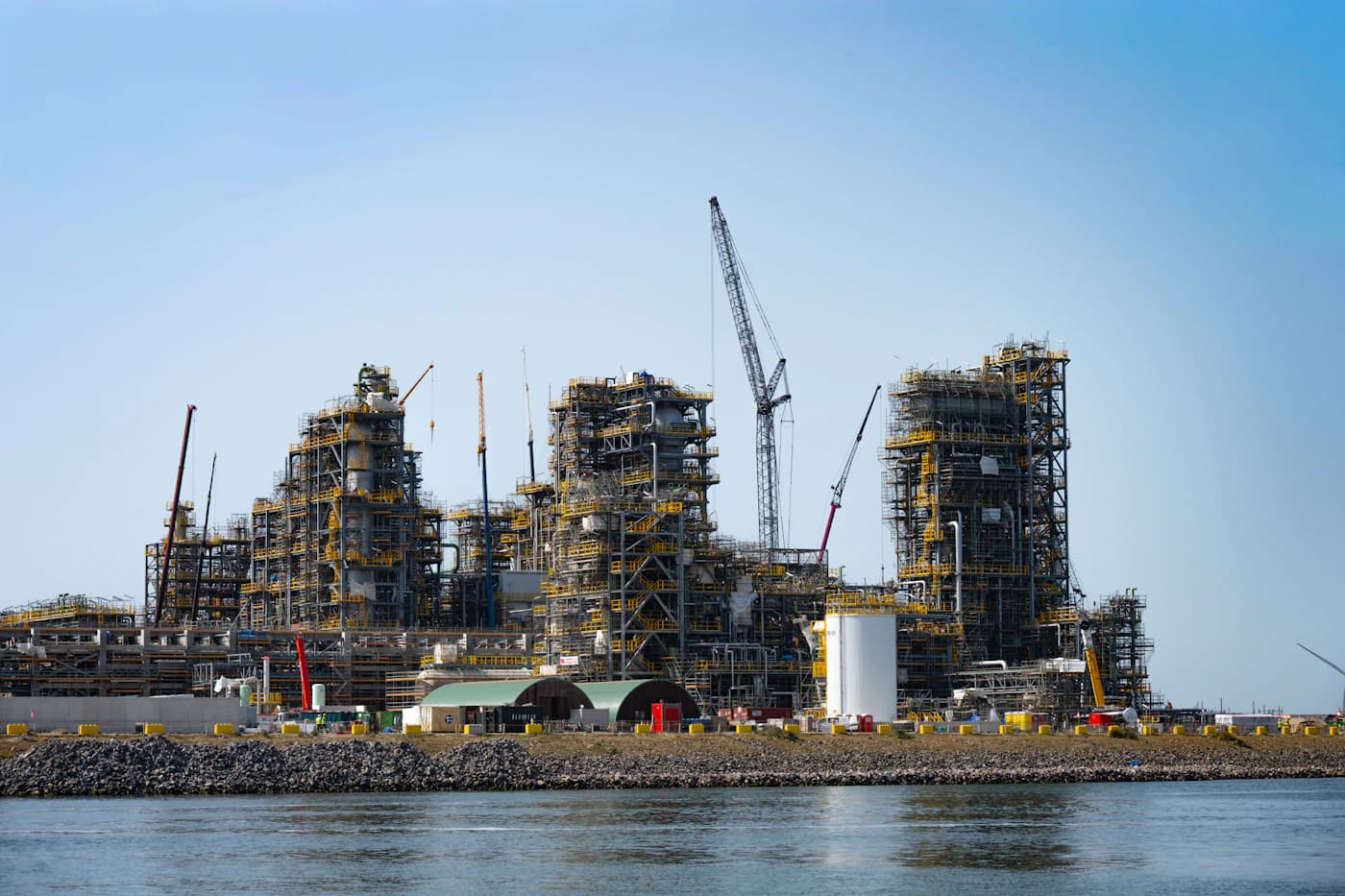 Cranes above the process units of a large plant under construction beside the water